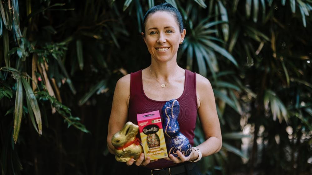 Steph Perkiss stands in front of some trees, holding an armful of Easter chocolates. She wears a red shirt and black pants and is smiling. Photo: Michael Gray